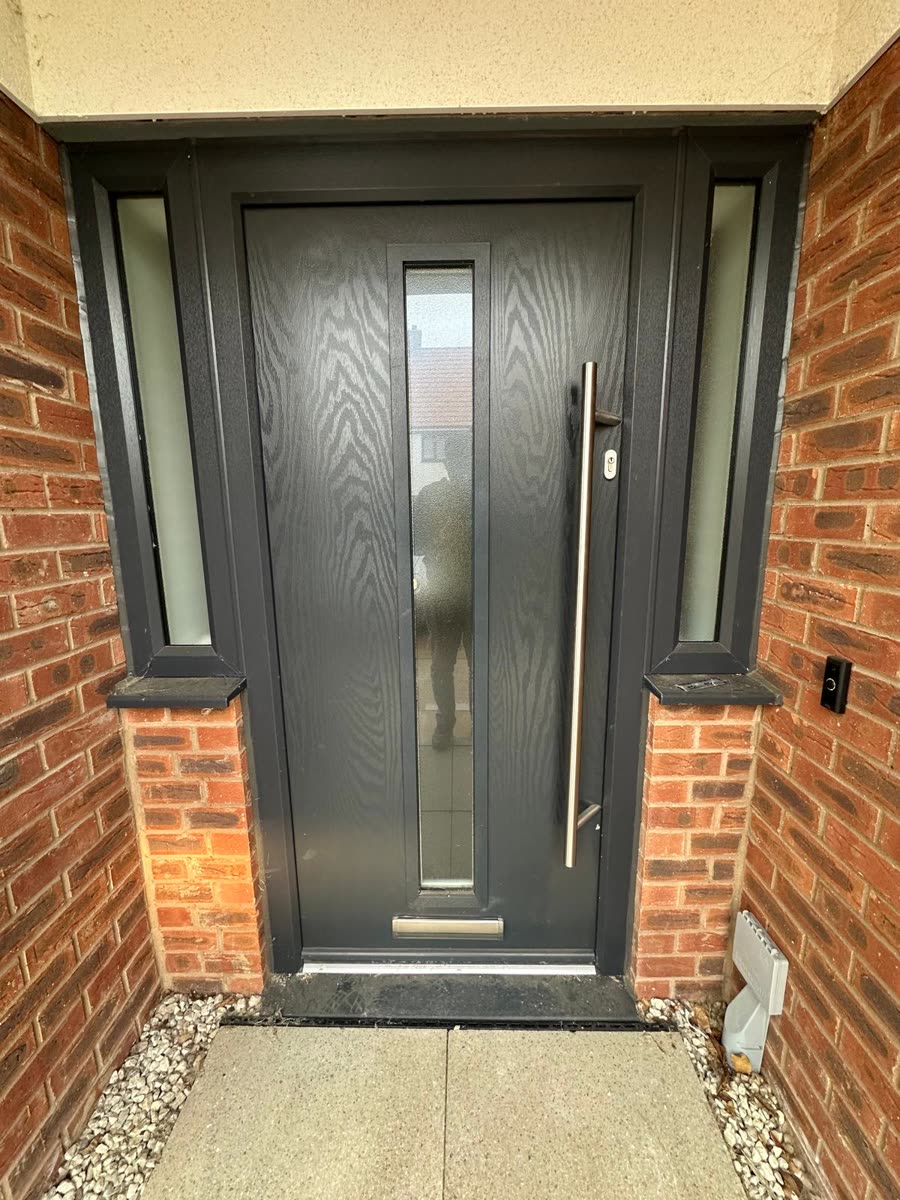 Anthracite grey composite front door with a long brushed steel handle and glazed side panels, fitted by URG