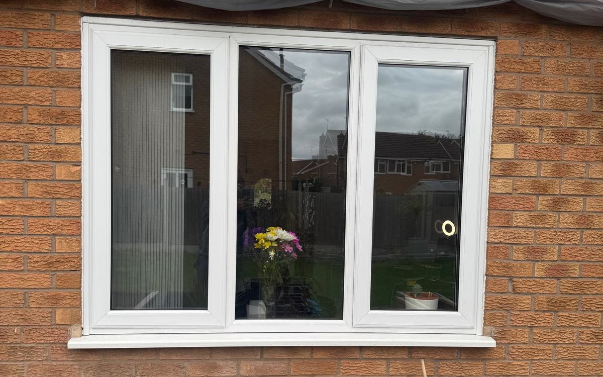 A white uPVC three-pane casement window with a matching sill, fitted by URG in a red brick house